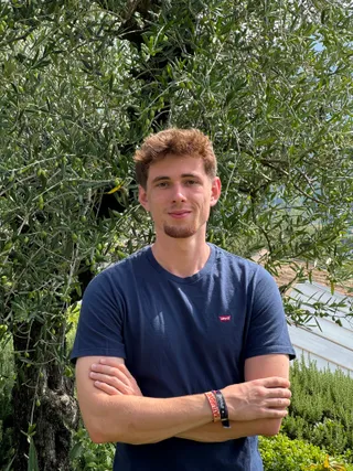 Frederik Mondel Portraitfoto – Gründer und Entwickler von AuxCampus mit verschränkten Armen vor Olivenbaum